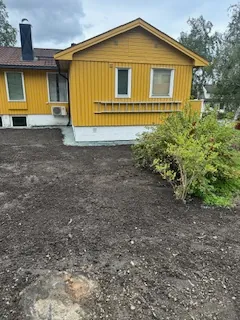 Gul enebolig med nysådd jord foran hagen og en busk til høyre.
